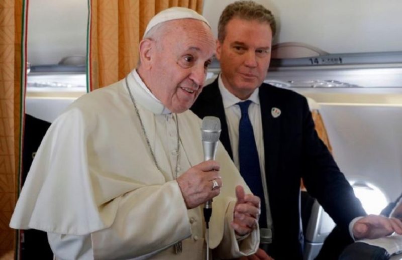 Picture of the pope with a microphone in his hand aboard the papal plane